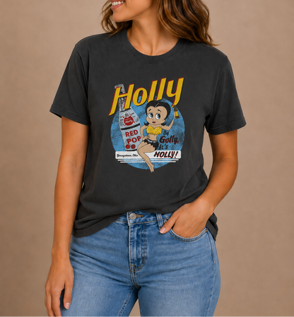 Woman wearing the By Golly, It's Holly! Tee featuring nostalgic Holly soda branding and retro-inspired artwork.