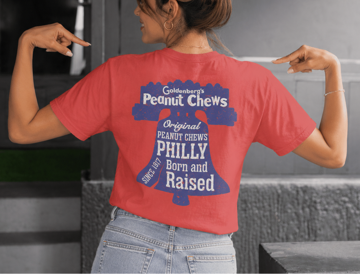 Female model pointing to the back graphic on the GOLDENBERG'S® PEANUT CHEWS® Since 1917 Liberty Bell Tee featuring the iconic Liberty Bell artwork.