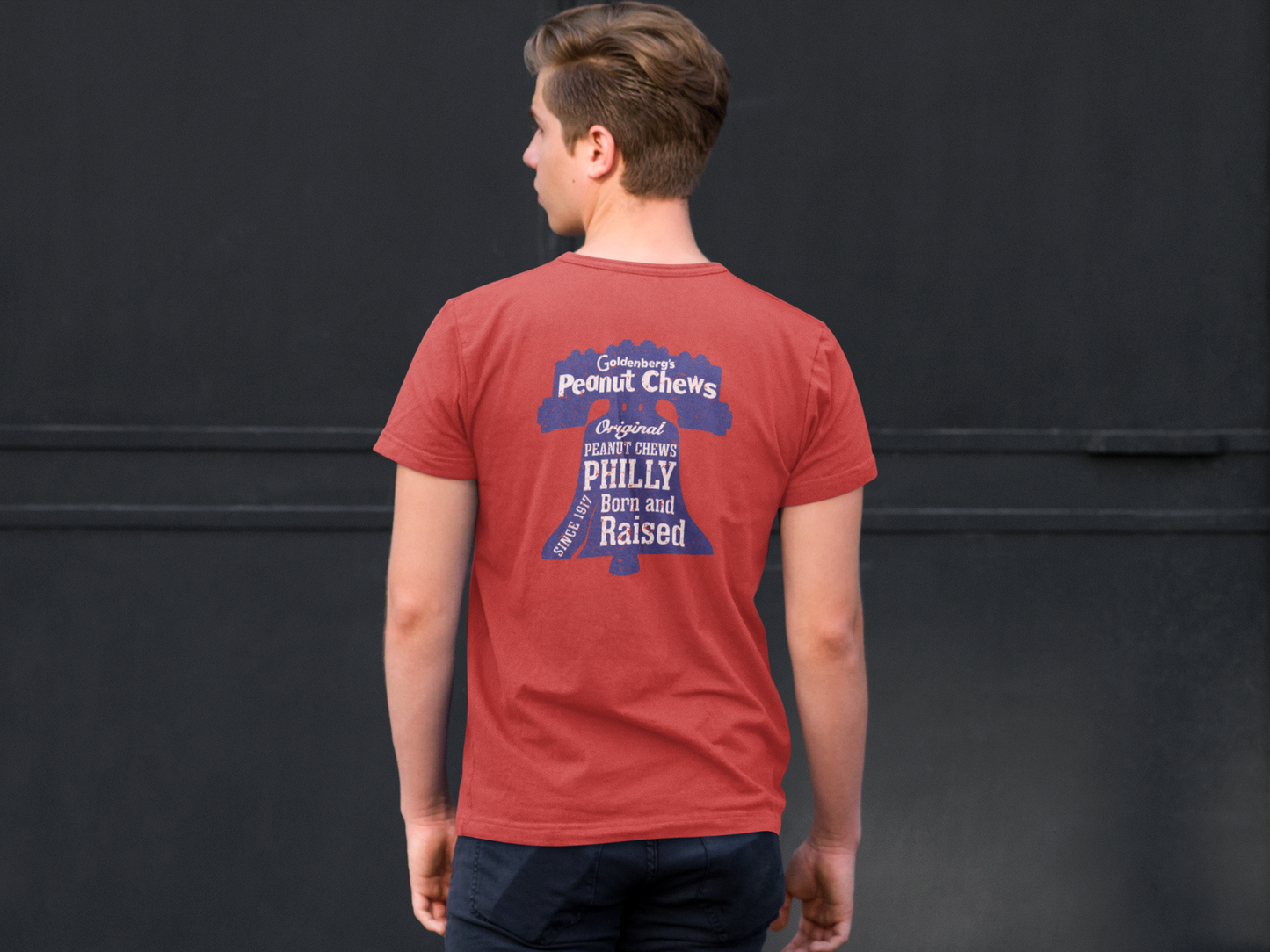 Male model wearing the back of the GOLDENBERG'S® PEANUT CHEWS® Since 1917 Liberty Bell Tee featuring the large Philly Born and Raised graphic.