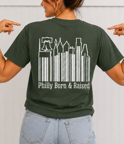 Female model wearing the back of the GOLDENBERG'S® PEANUT CHEWS® Philly Born & Raised Skyline Barcode Tee and pointing to the Philadelphia skyline graphic.