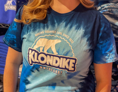 Female model wearing a Klondike® Making Squares Cool Since 1922 unisex blue tie-dye T-shirt featuring the iconic Klondike polar bear logo and retro frozen treat graphic design.