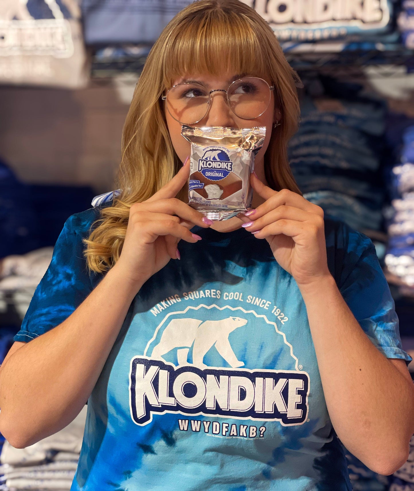 Female model wearing a Klondike® Making Squares Cool Since 1922 unisex blue tie-dye T-shirt featuring the iconic Klondike polar bear logo and retro frozen treat graphic design.