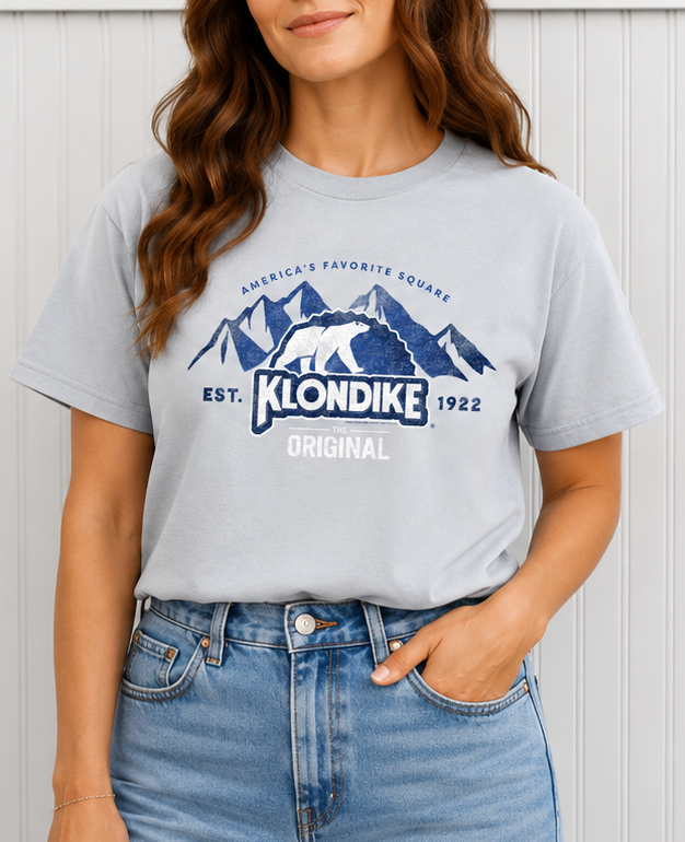 Female model wearing a Klondike® The Original Since 1922 Vintage Graphic Tee in light gray with distressed Klondike branding, mountain artwork, and classic polar bear logo.