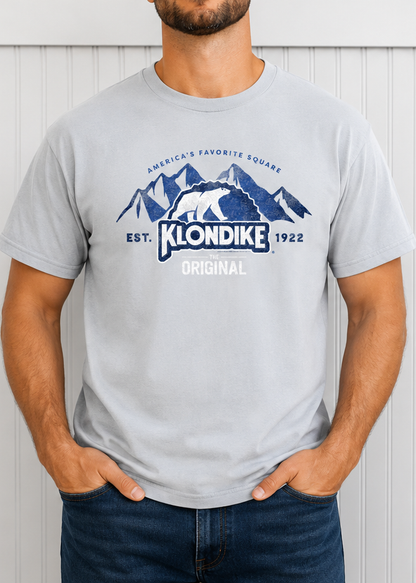 Male model wearing a Klondike® The Original Since 1922 Vintage Unisex Graphic Tee in light gray featuring the iconic polar bear logo and mountain-inspired retro design.