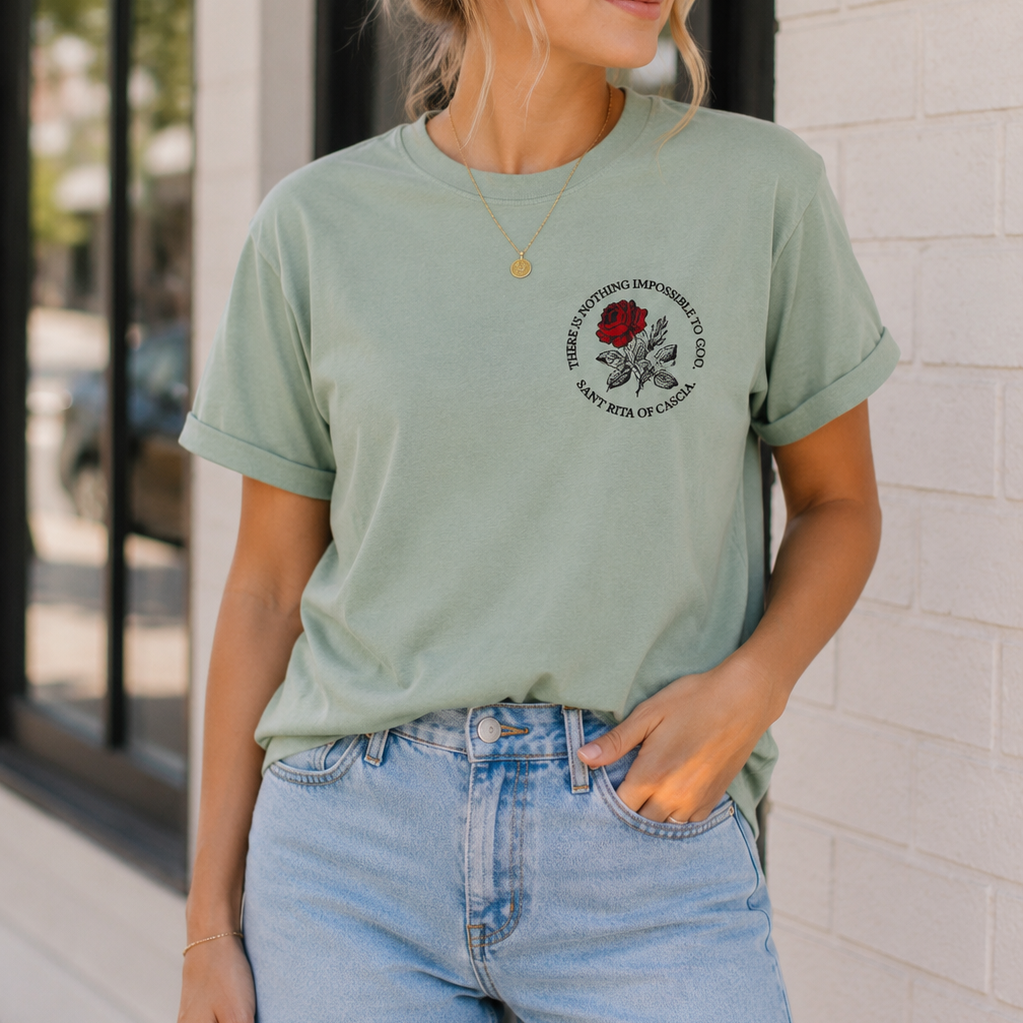 Woman wearing the Saint Rita of Cascia "There Is Nothing Impossible to God" unisex graphic T-shirt featuring the red rose chest design.