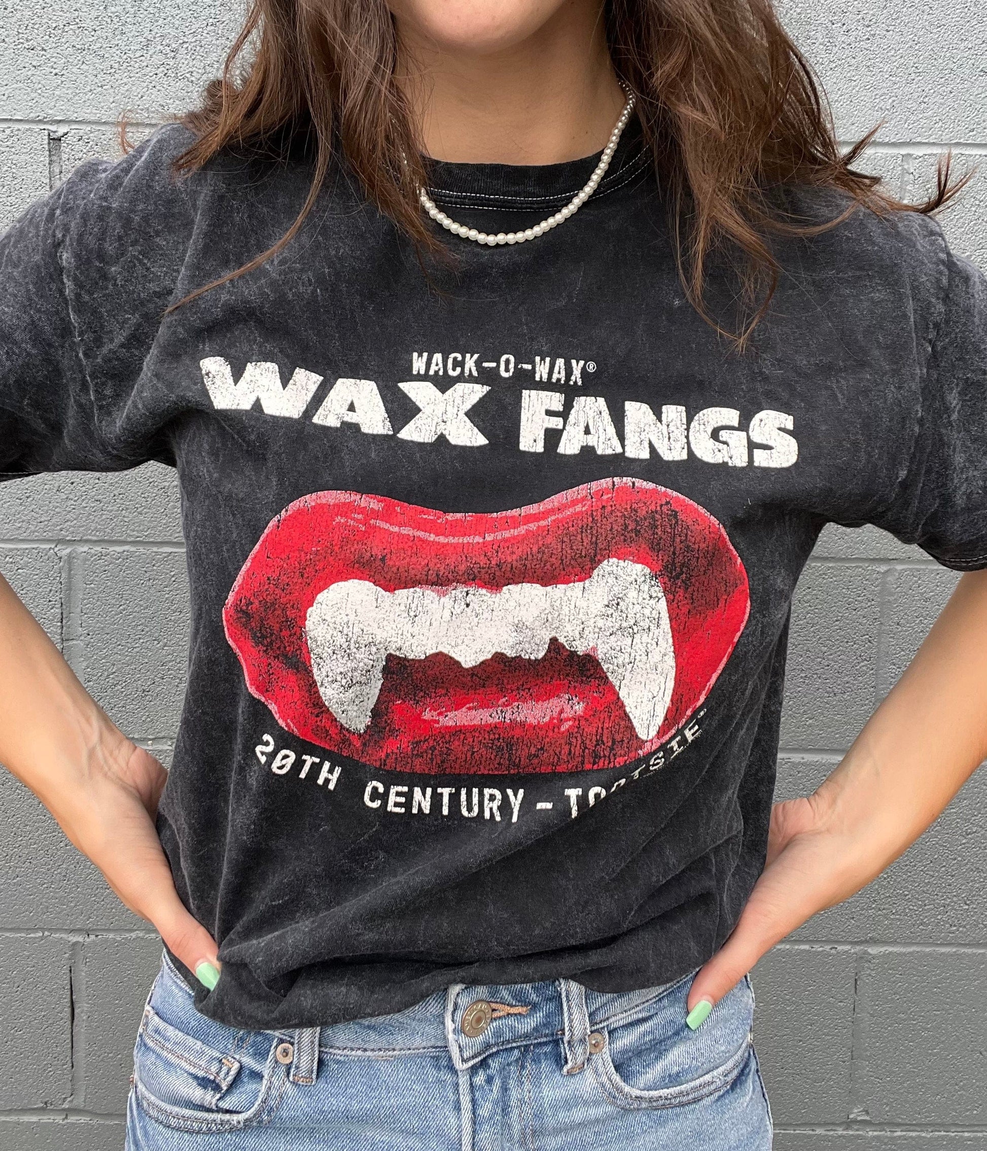 Woman wearing a Wack-O-Wax FANGS Black Mineral Wash Tee featuring nostalgic wax vampire fangs candy artwork.