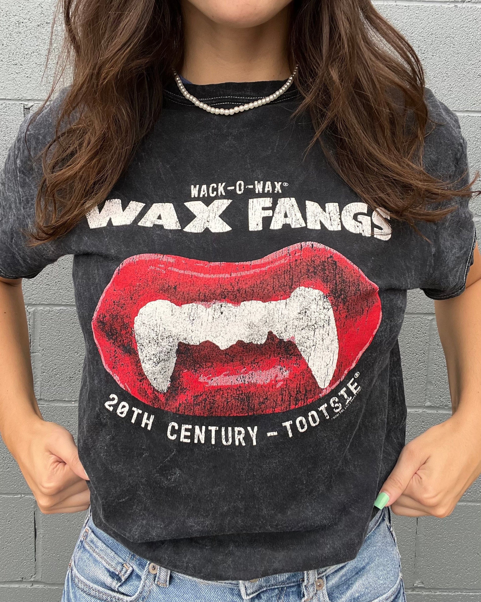 Woman wearing a Wack-O-Wax FANGS Black Mineral Wash Tee featuring nostalgic wax vampire fangs candy artwork.